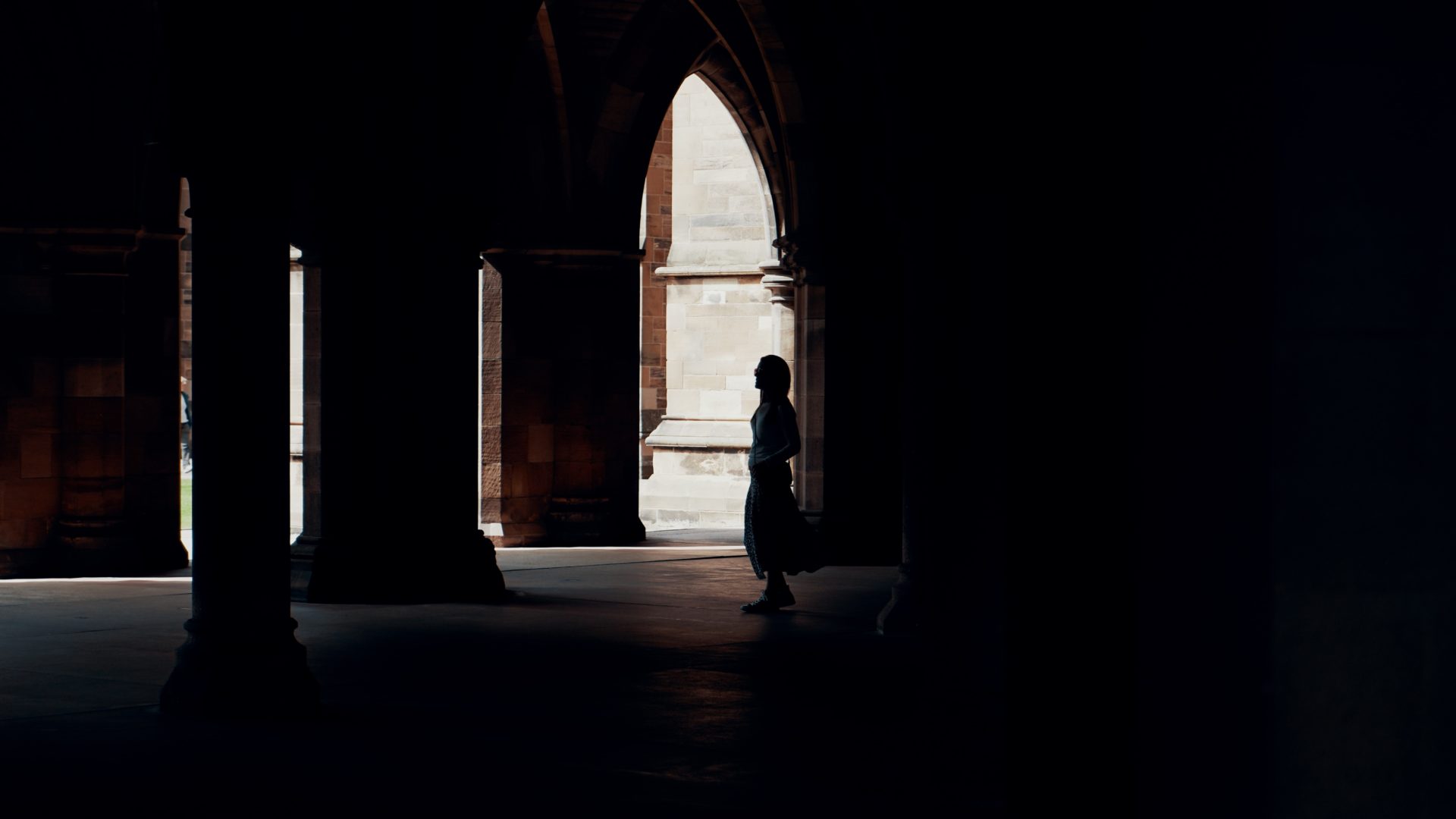 A person stands in the shadows of the arches on the University of Glasgow campus
