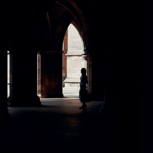 A person stands in the shadows of the arches on the University of Glasgow campus