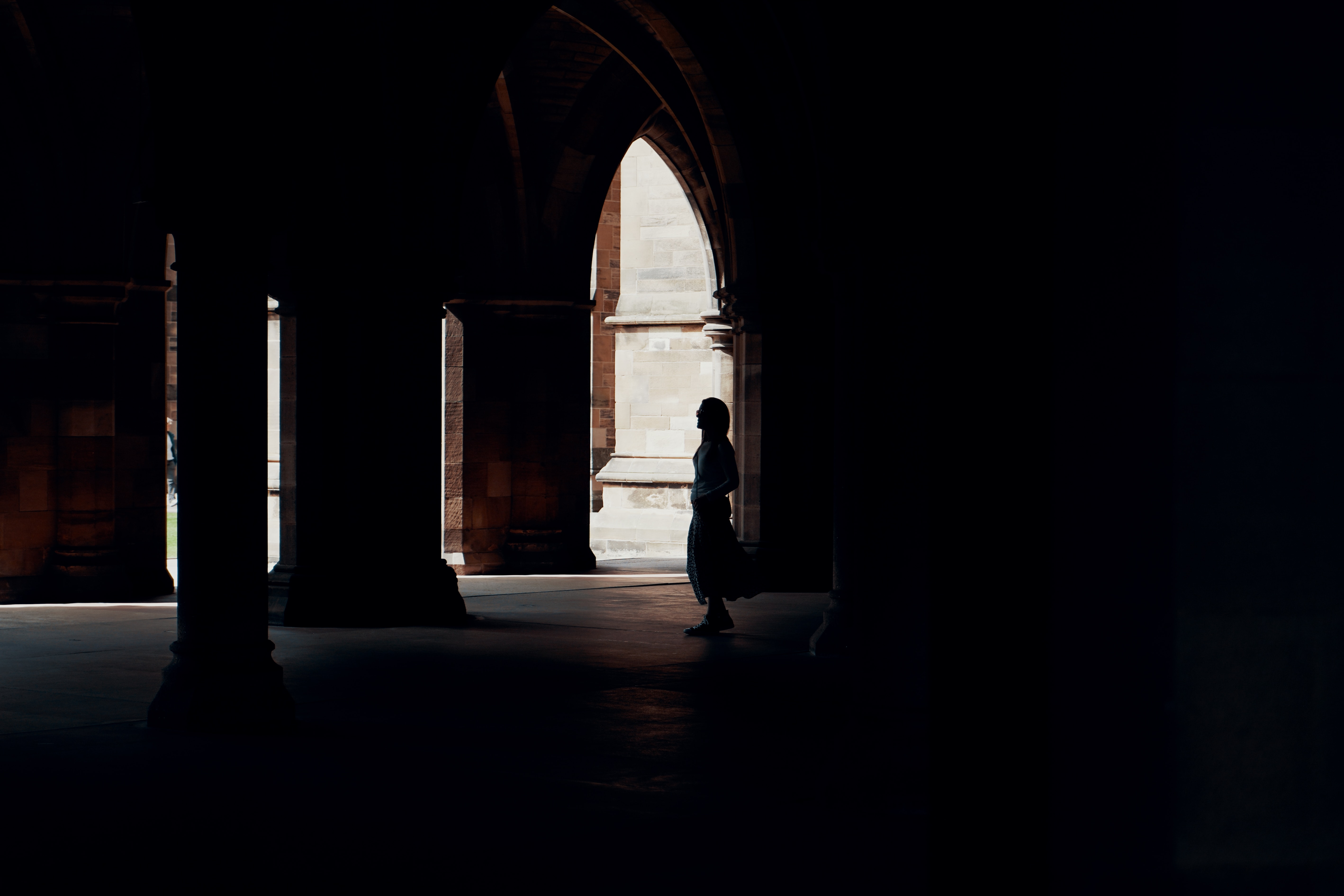 A person stands in the shadows of the arches on the University of Glasgow campus