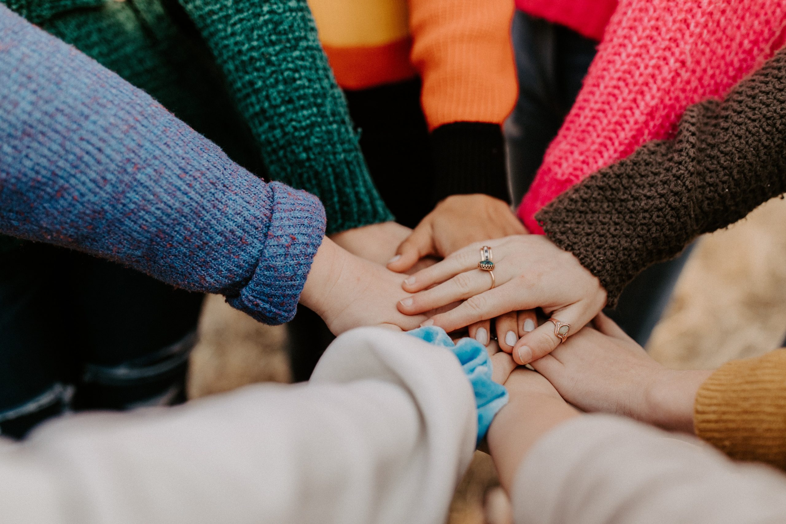 People gathered in a circle, placing their hands on top of one another.